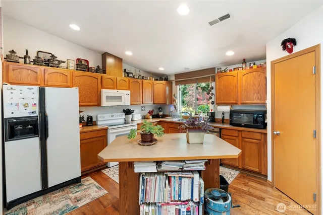 a kitchen with stainless steel appliances granite countertop a refrigerator a sink dishwasher a stove and white countertops with wooden floor