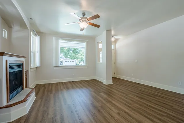 an empty room with wooden floor chandelier fan and windows