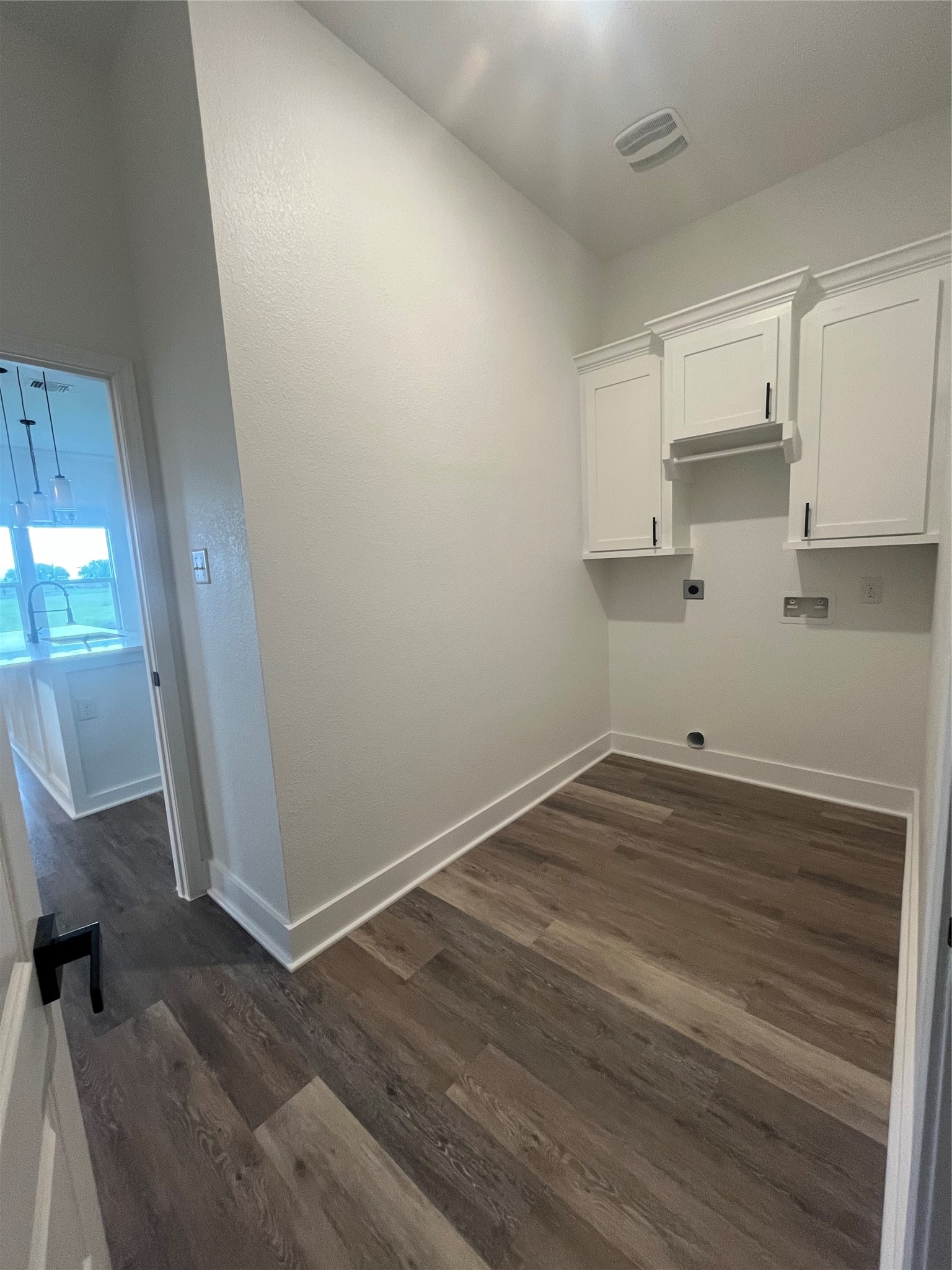 33416 FM 521 Road Angleton, TX 77515 - Photo 11 of 21 This photo shows a small laundry or utility room with light and medium gray/wood water proof plank flooring. It features white cabinetry and space for appliances, with an adjacent view into a well-lit kitchen area.