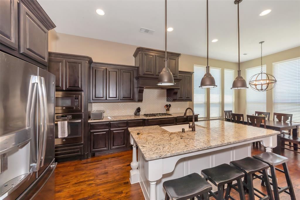 1001 West Bluff Way Roanoke, TX 76262 - Photo 12 of 40 Kitchen with appliances with stainless steel finishes, dark brown cabinetry, light stone counters, tasteful backsplash, and a breakfast bar area