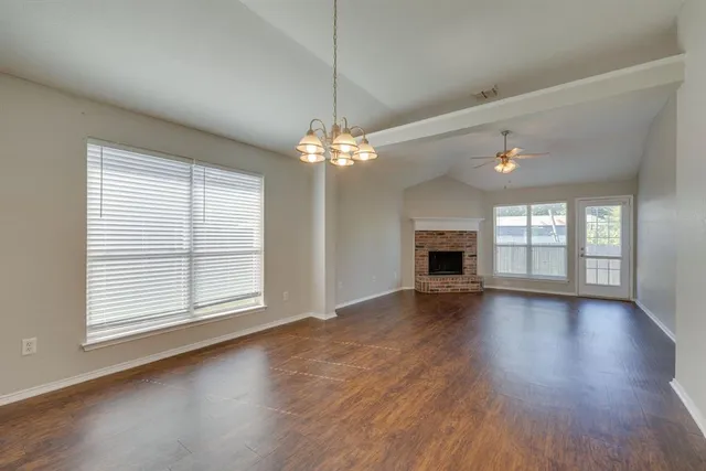 an empty room with wooden floor fireplace and windows