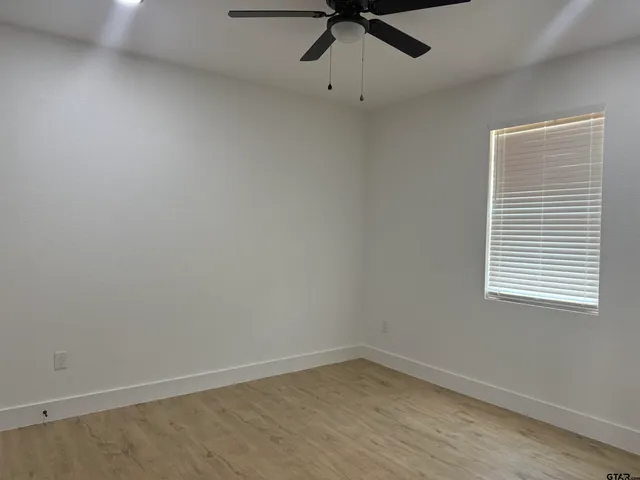 an empty room with chandelier fan and windows