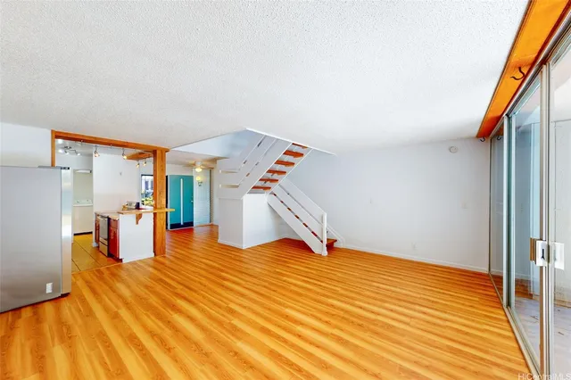 a view of an empty room with wooden floor and stairs