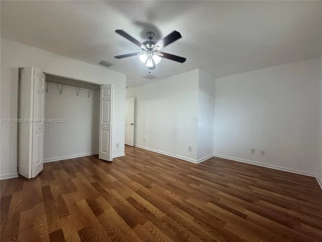 a view of an empty room with wooden floor and a ceiling fan