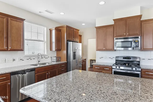 a kitchen with stainless steel appliances granite countertop a sink stove refrigerator and cabinets