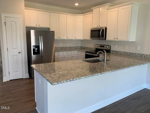 a kitchen with stainless steel appliances granite countertop a sink a microwave a refrigerator and white cabinets