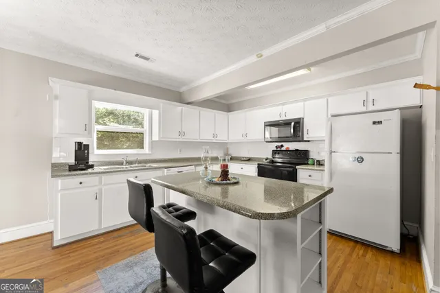a kitchen with stainless steel appliances granite countertop a stove a sink dishwasher a refrigerator white cabinets and wooden floor next to a window