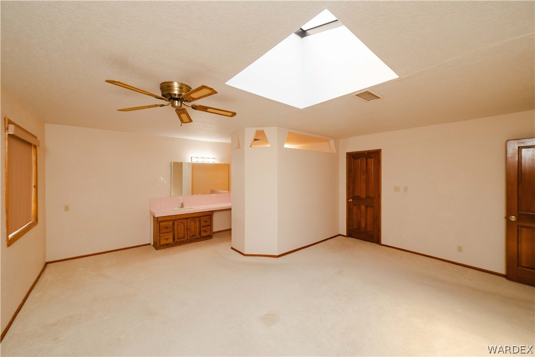 2100 East Valley View Road Kingman, AZ 86409 - Photo 20 of 53 Spacious room featuring a skylight, ceiling fan, built-in vanity with a sink, and wood-finish doors