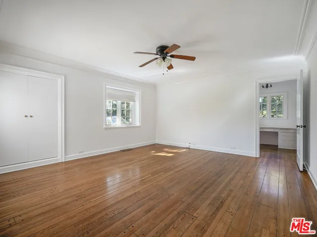 an empty room with wooden floor chandelier fan and windows