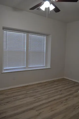 a view of an empty room with wooden floor and fan