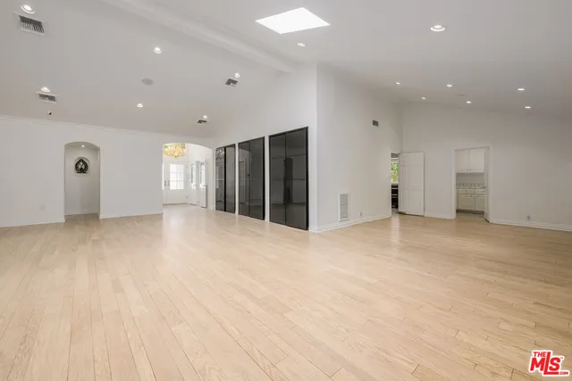a view of an empty room with wooden floor and a kitchen
