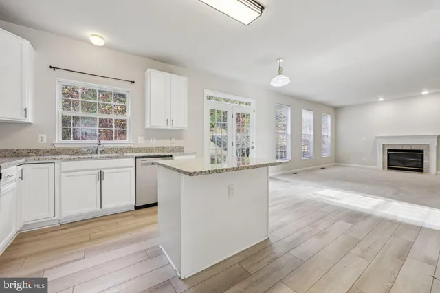 a large kitchen with granite countertop a stove a sink a refrigerator and white cabinets with wooden floor