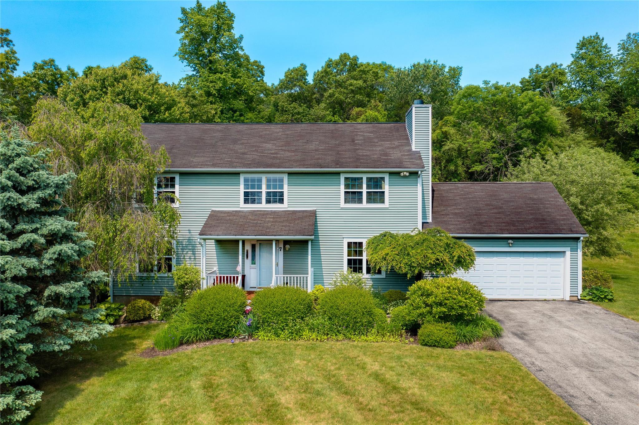 View of front of property featuring a garage, asphalt driveway, a chimney, a front yard, and covered porch