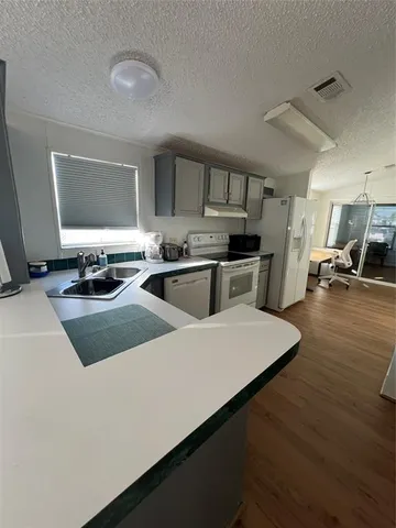 a kitchen with stainless steel appliances a sink a stove a refrigerator white cabinets and wooden floor