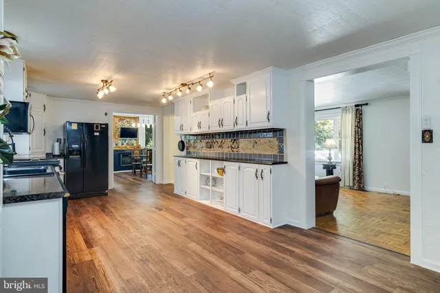 a kitchen with stainless steel appliances kitchen island granite countertop a refrigerator oven a sink dishwasher and white cabinets with wooden floor