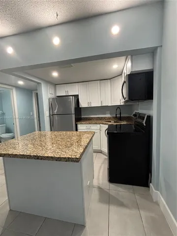 a kitchen with kitchen island granite countertop a sink a counter top space appliances and cabinets