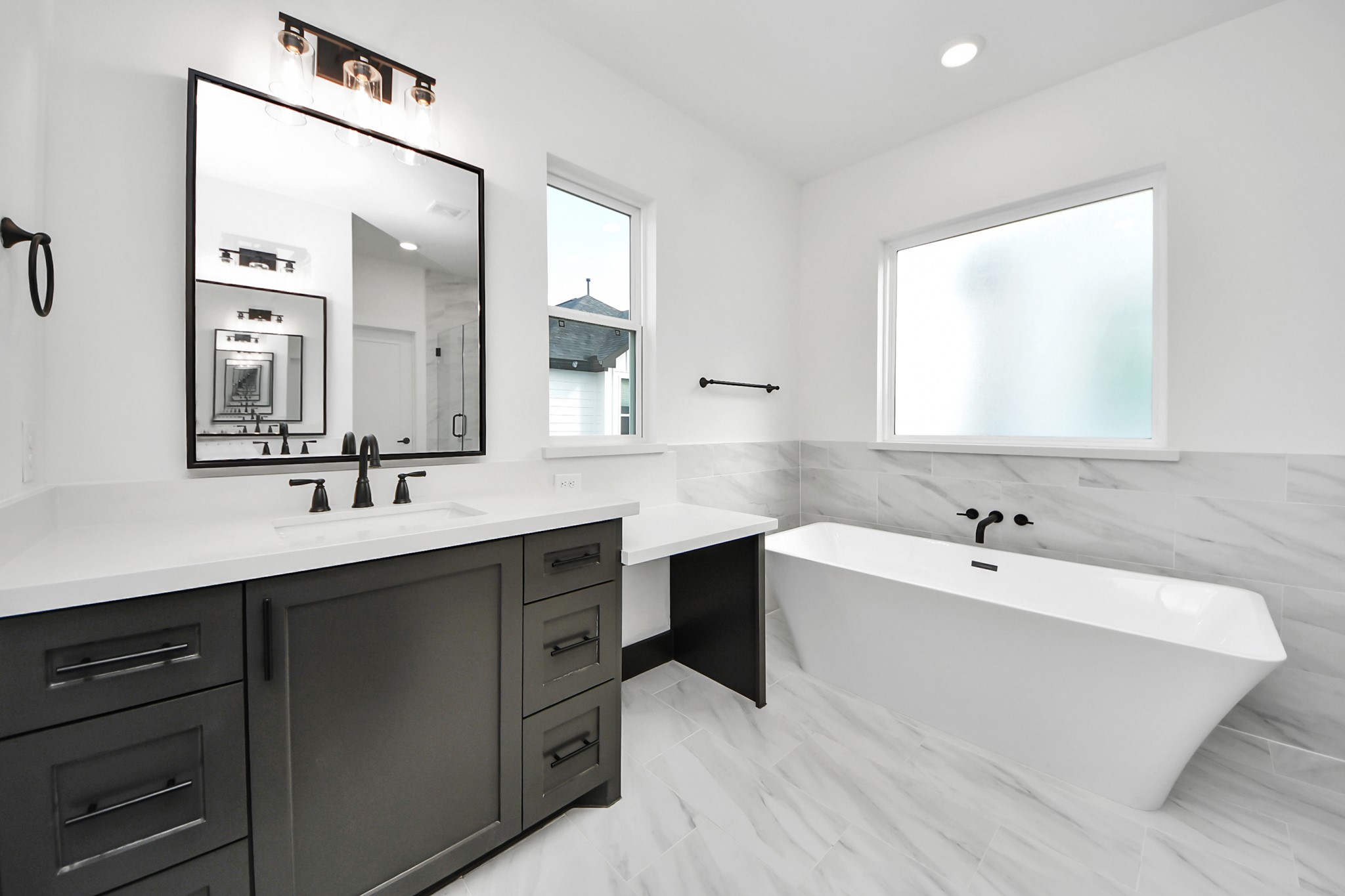 723 Marcella Street, Unit D Houston, TX 77091 - Photo 19 of 22 This is a modern, stylish bathroom featuring a sleek freestanding bathtub, a large vanity with dual sinks, and elegant black fixtures. The space is bright with a frosted window and a sophisticated monochrome color scheme.