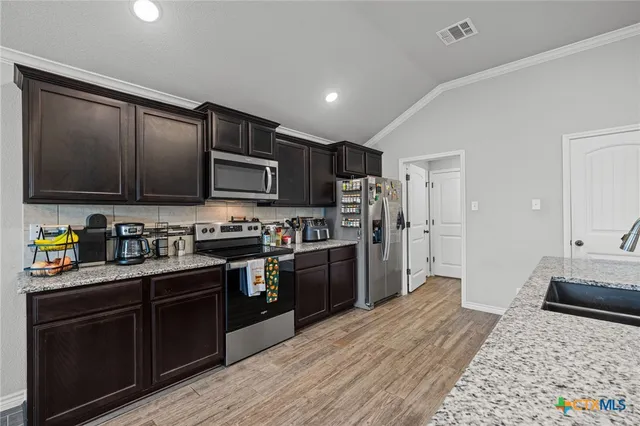 a kitchen with granite countertop wooden cabinets a stove top oven and stainless steel appliances