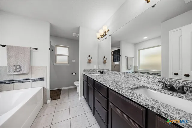 a spacious bathroom with a granite countertop double vanity sink a mirror and a bathtub