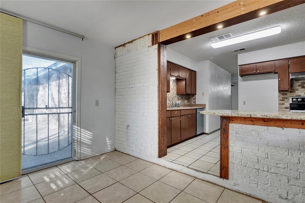 210 Slaughter Street Arlington, TX 76011 - Photo 18 of 33 Kitchen featuring light tile patterned flooring, brick wall, tasteful backsplash, a peninsula, and appliances with stainless steel finishes