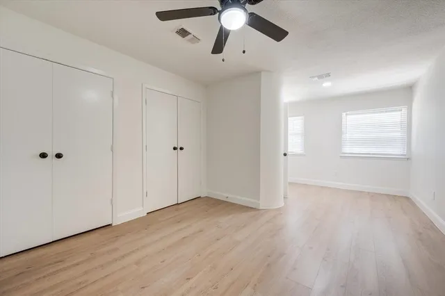 an empty room with wooden floor chandelier fan and windows