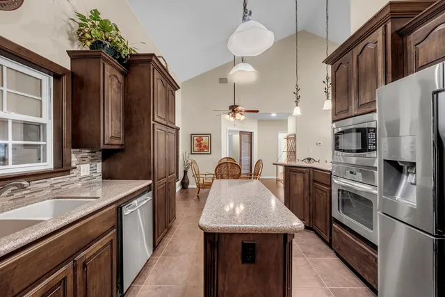 a kitchen with stainless steel appliances kitchen island granite countertop a refrigerator a stove and a sink with wooden floor