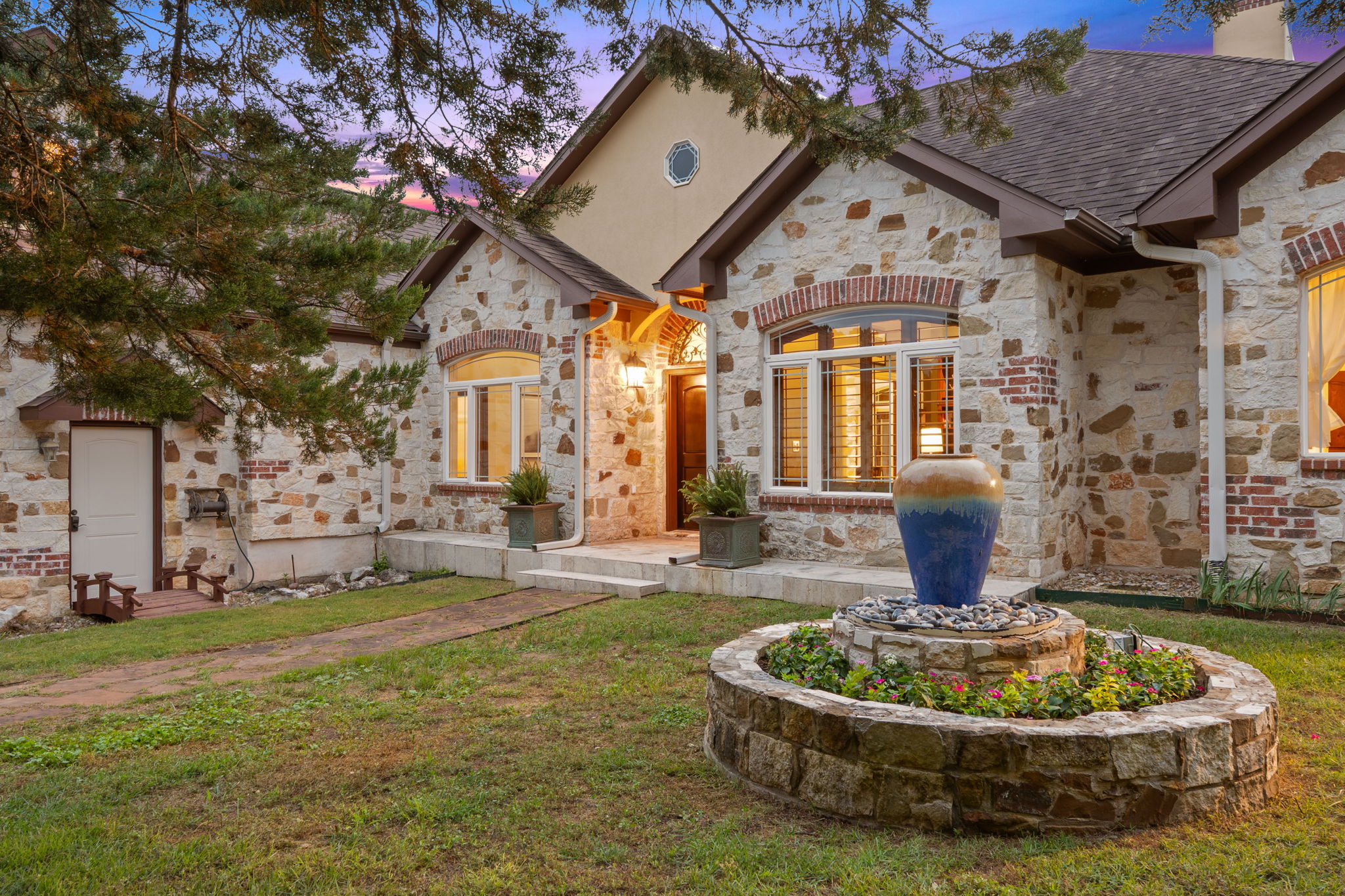 8121 Bluff Trail Austin, TX 78737 - Photo 3 of 40 A stone-clad residence with architectural appeal, featuring a decorative outdoor fountain and well-maintained landscaping.