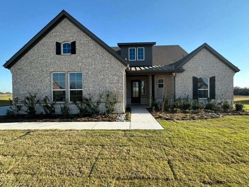 View of front of home with brick siding, a front lawn, a standing seam roof, and covered porch