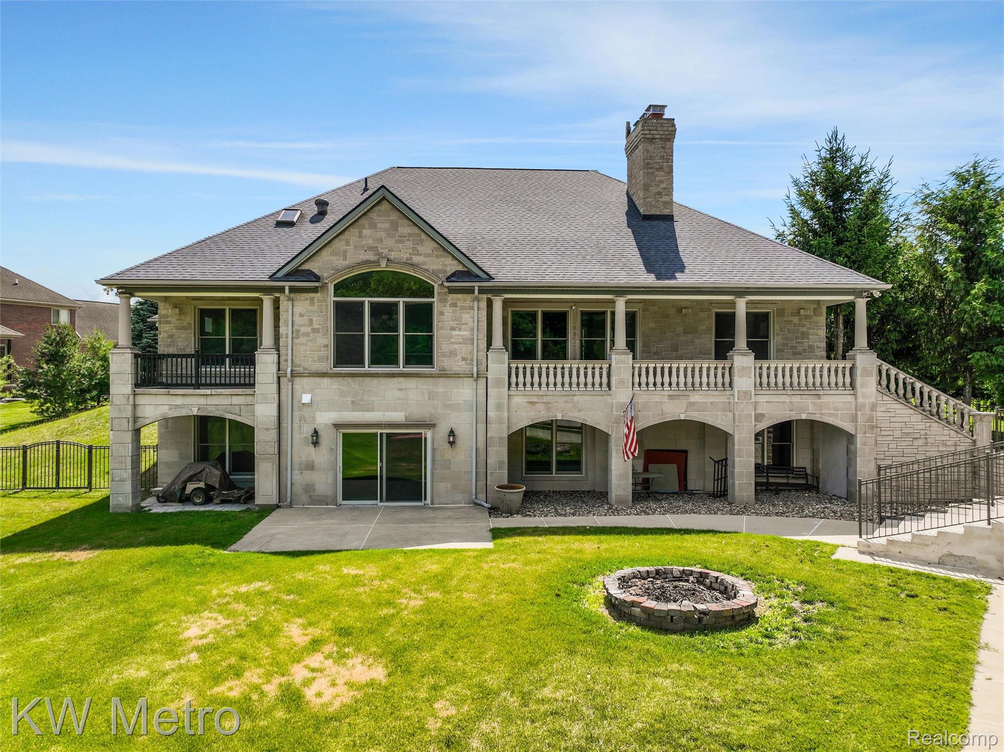 65884 Windrose Court Ray, MI 48096 - Photo 7 of 82 Stone facade residence featuring a multi-level design with a covered patio, upper-level balcony, and an outdoor fire pit