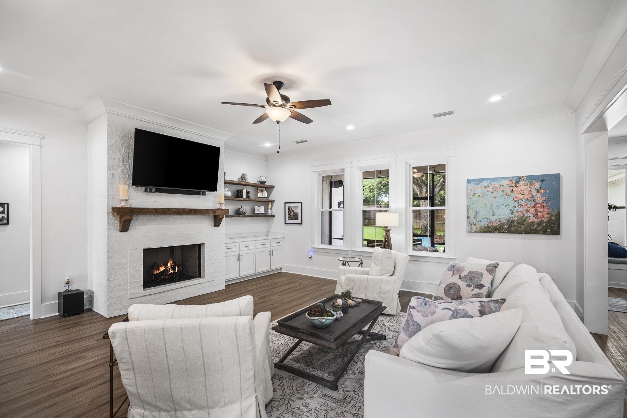 21702 Pillars Street Fairhope, AL 36532 - Photo 6 of 54 Living area featuring a white brick fireplace with a wood mantel, built-in shelving, white cabinetry, wood-finish flooring, and a ceiling fan