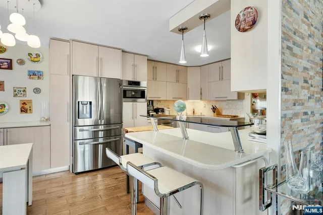 a kitchen with stainless steel appliances granite countertop a refrigerator a sink dishwasher a dining table and chairs with wooden floor