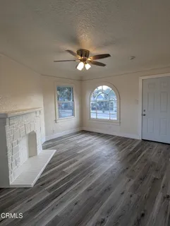 a view of an empty room with chandelier fan and wooden floor