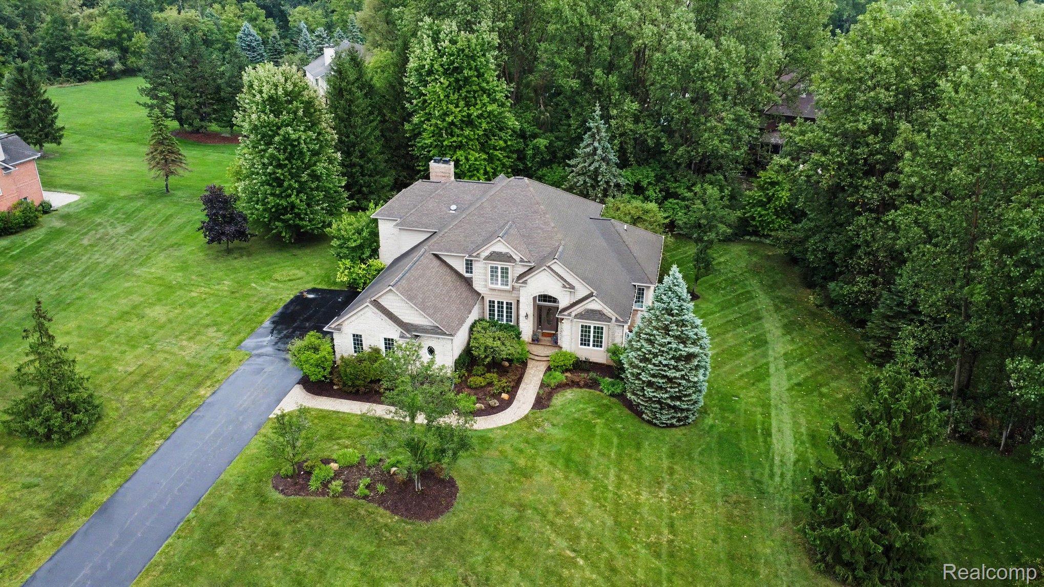 4875 Green Meadow Lane Rochester, MI 48306 - Photo 60 of 60 Stucco exterior residence featuring a multi-gabled roof, extensive landscaping, and a paved driveway, surrounded by mature trees