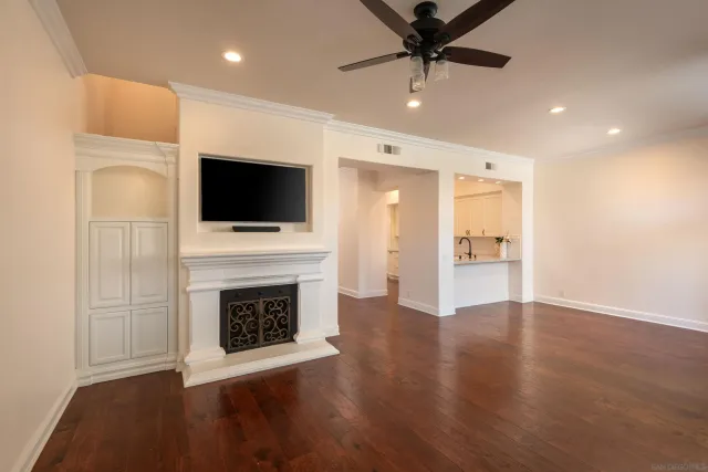 a view of a livingroom with a fireplace a ceiling fan and steel kitchen view