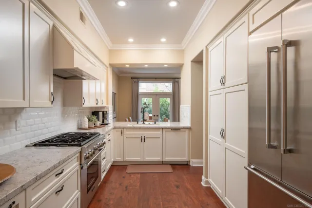 a kitchen with granite countertop a refrigerator a sink dishwasher a stove and white cabinets with wooden floor