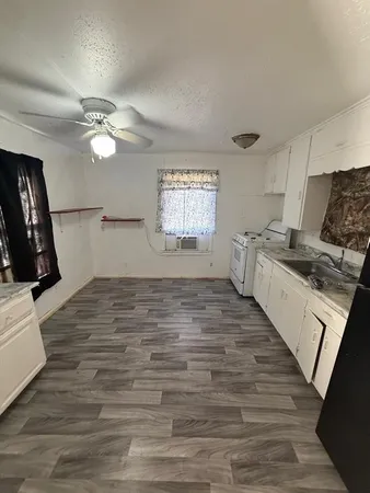 a kitchen with granite countertop a stove a sink and white cabinets with wooden floor