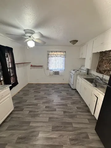 a kitchen with granite countertop a stove a sink and white cabinets with wooden floor