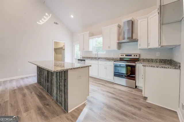 a kitchen with stainless steel appliances granite countertop a stove top oven a sink dishwasher and white cabinets with wooden floor