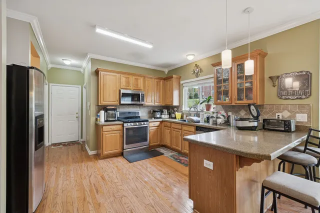 a kitchen with stainless steel appliances granite countertop a refrigerator a sink dishwasher a stove and a dining table with wooden floor