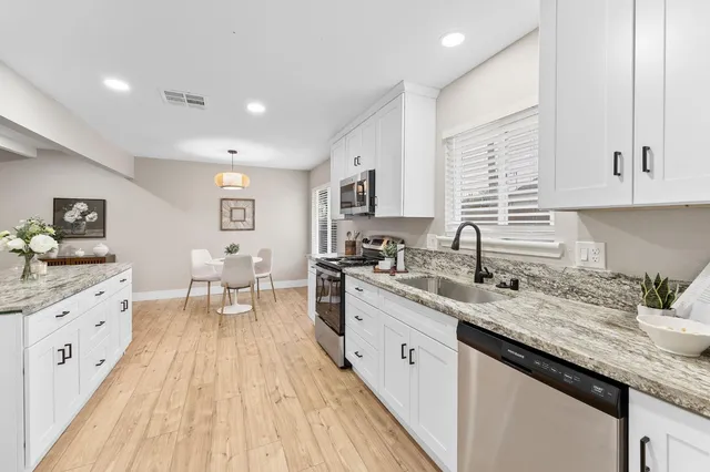 a kitchen with granite countertop sink stove and white cabinets with wooden floor