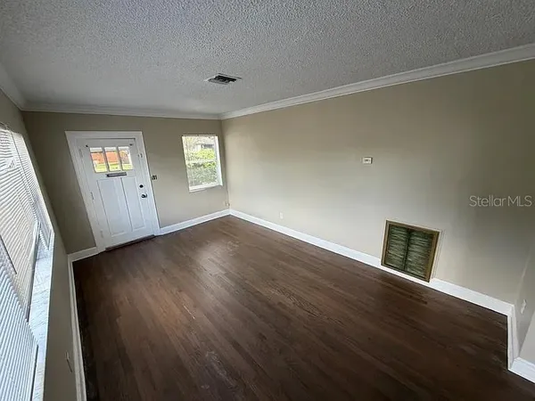a view of an empty room with wooden floor and a window