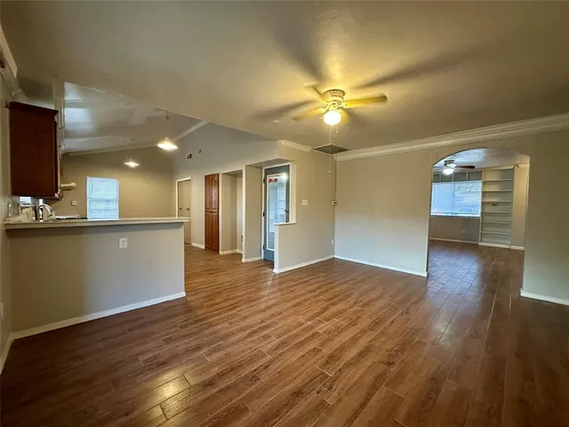 a view of an empty room and kitchen with wooden floor