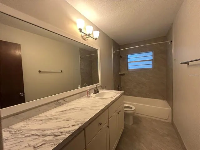 a bathroom with a granite countertop sink a toilet a mirror and bathtub