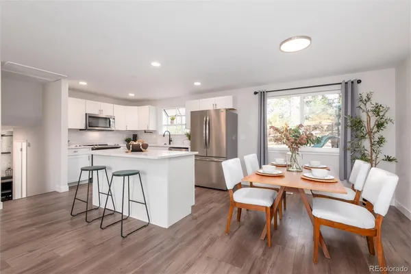 a open dining room with stainless steel appliances a dining table wooden floor and a large window