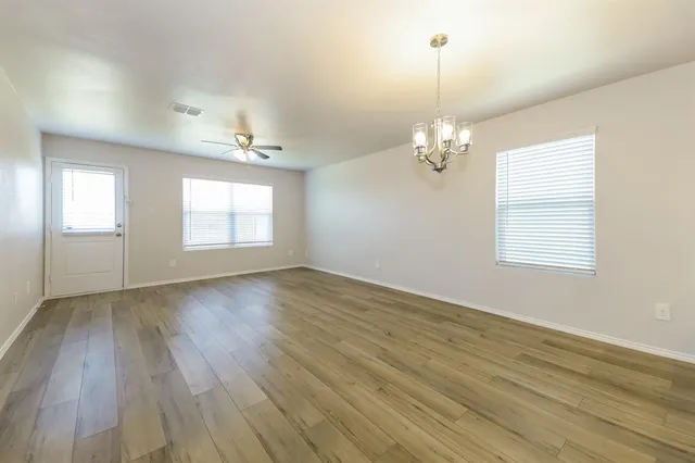 an empty room with wooden floor chandelier and windows