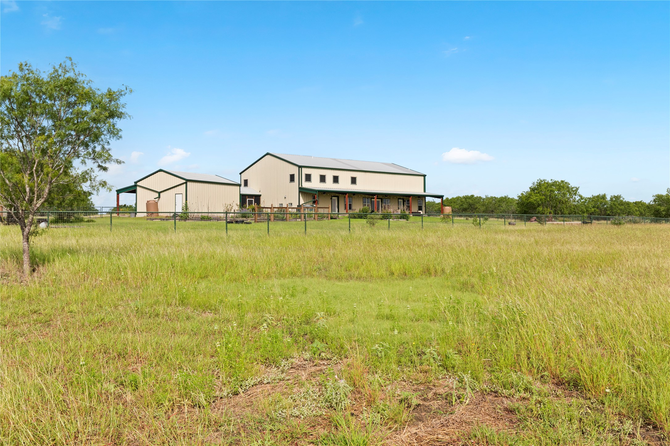 1293 Pioneer Road Seguin, TX 78155 - Photo 37 of 40 A spacious barn-style residence sits nestled amidst a vast, open field, surrounded by verdant trees under an expansive sky.