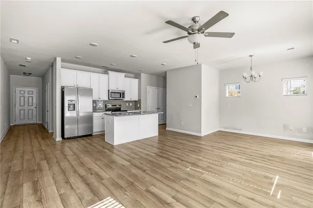 a kitchen with stainless steel appliances granite countertop a refrigerator a stove a sink and white cabinets with wooden floor