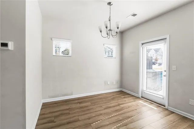 an empty room with wooden floor chandelier and windows