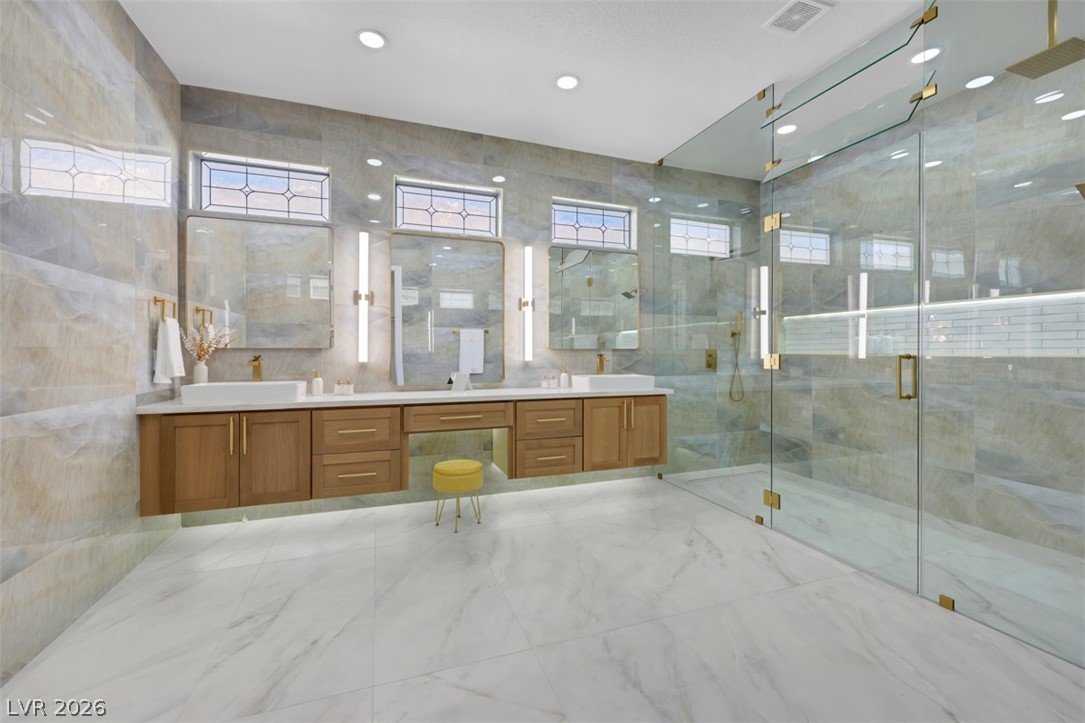 5015 Rivedro Street Las Vegas, NV 89135 - Photo 35 of 91 A well-appointed primary bathroom showcases dual vanities, contemporary fixtures, and an expansive glass-enclosed shower.
