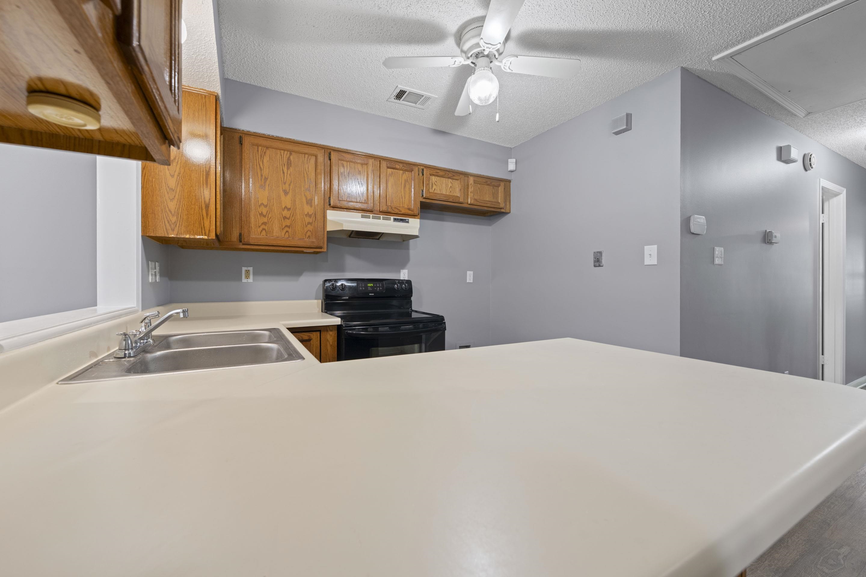 2252 Mangum Road Memphis, TN 38134 - Photo 11 of 23 Kitchen featuring wood cabinetry, a stainless steel double basin sink, light-toned countertops, and a black electric range